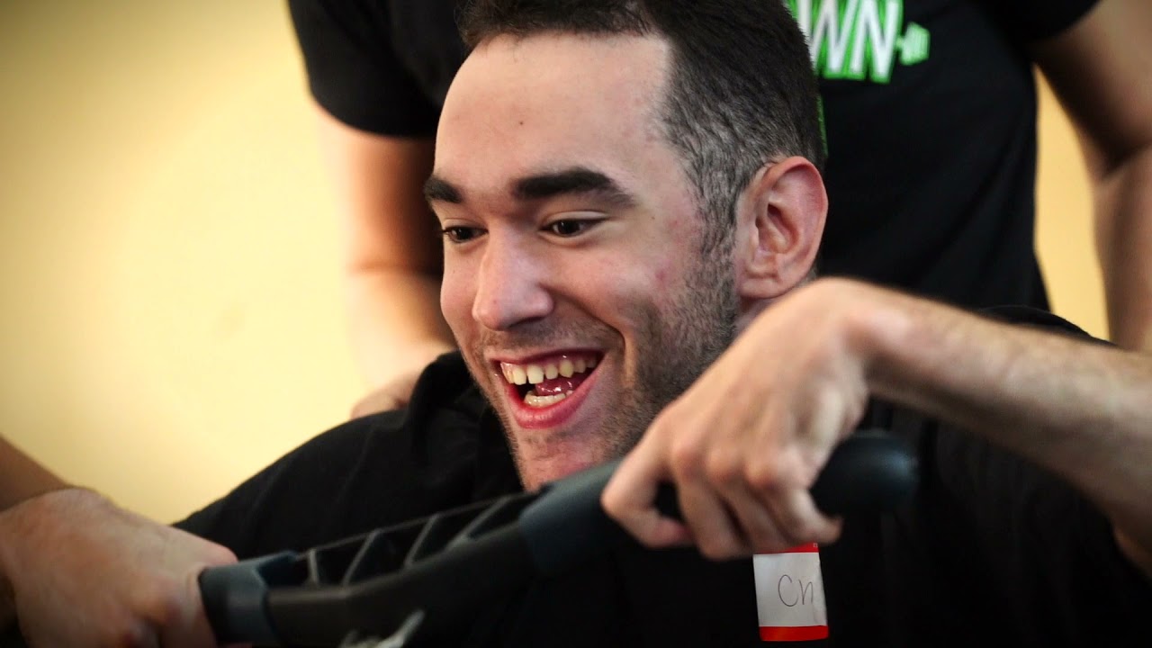 A man with dark hair and a light complexion smiles widely while gripping onto exercise equipment